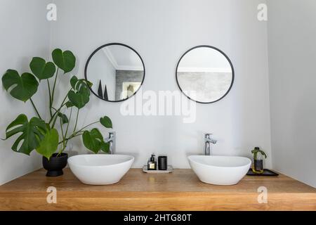 Specchi di forma circolare montati sulla parete sotto i lavandini nella stanza da bagno in casa Foto Stock