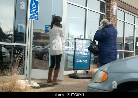 Donna che mette su una maschera che va all'interno per il vaccino covid e lavoratore che tiene la porta. Oakdale Minnesota, Stati Uniti Foto Stock