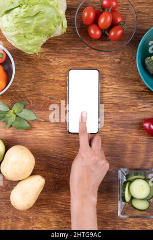 Direttamente sopra il colpo della mano ritagliata usando lo smart phone fra il cibo vario sul tavolo, spazio della copia Foto Stock