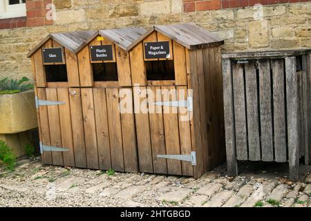 Tre bidoni di riciclaggio in legno con accanto un bidone per rifiuti non riciclabili. Carta, riviste, bottiglie di vetro e plastica riciclano le unità accanto al Foto Stock