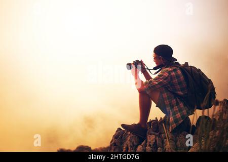 La fotografia è un affare d'amore con la natura. Scatto di un giovane fotografo che scatta una foto di un paesaggio nebbia dalla cima di una montagna. Foto Stock