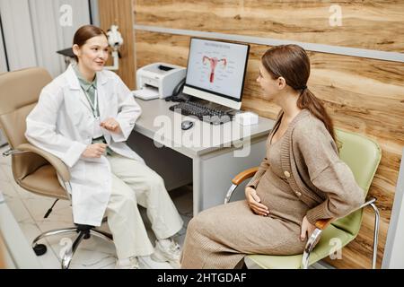 Ritratto di ostetricia femminile che parla con la giovane donna incinta durante la consultazione in ufficio medico Foto Stock