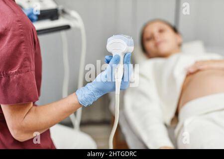 Primo piano di una dottore che tiene il trasduttore a ultrasuoni durante l'esame di una giovane donna incinta in clinica, spazio copia Foto Stock