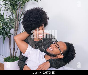 Primo piano ritratto di coppia abbraccio e sorridente giovane marito felice e moglie con capelli Afro stile a casa. Foto Stock