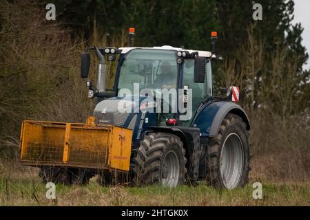 Trattore FENDT 720 dotato di una scatola di trasporto con attacco rapido Twose gialla, che procede lungo una corsia di campagna Foto Stock