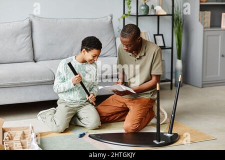 Ritratto a tutta lunghezza di uomo afro-americano che monta i mobili a casa con la figlia aiutare Foto Stock