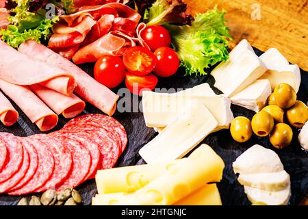 Salumi, antipasti con assortimento di salumi, formaggi, camembert e olive su tavola di legno. Vari tipi di carne e salsicce su legno Foto Stock