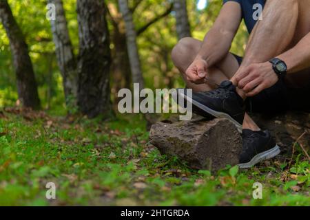 Uomo che lega le sue scarpe nel parco all'aperto, intorno alla foresta, querce erba verde giovane atleta resistente atleta. Allenarsi atleta corsa atletica Foto Stock