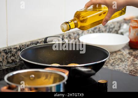 Scatto corto di una donna che versa l'olio di cottura dalla bottiglia alla padella in stufa Foto Stock