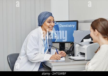 Vista laterale ritratto di dentista femmina sorridente consulente paziente in ufficio presso la clinica dentale moderna Foto Stock