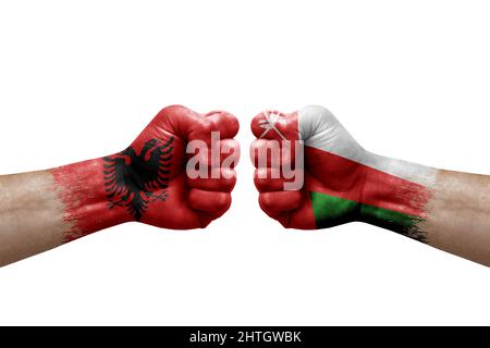 Due mani si pugno l'una all'altra su sfondo bianco. Bandiere di paese dipinte pugni, conflitto concetto di crisi tra albania e oman Foto Stock