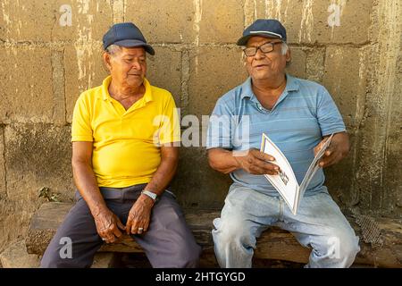 Due anziani latini seduti su un giornale e leggendo un documento Foto Stock