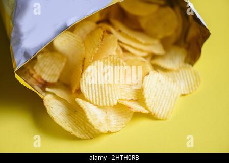 Anche di patate su sfondo giallo, patata chips è snack in sacchetto confezionato in plastica pronto a mangiare e cibi grassi o spazzatura cibo Foto Stock