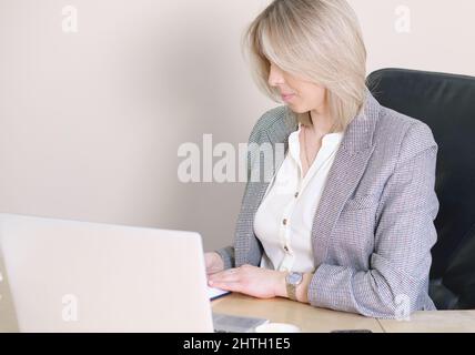 donna seduta alla scrivania tenendo penna scrittura in blocco note indossare abiti formali in ufficio al chiuso. pianificazione nuovo business startup. investitore business femminile Foto Stock