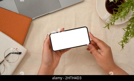 Overhead shot, mani femminili che tengono il telefono cellulare sopra lo spazio di lavoro minimo. Guardare video, giocare, guardare qualcosa su internet. Foto Stock