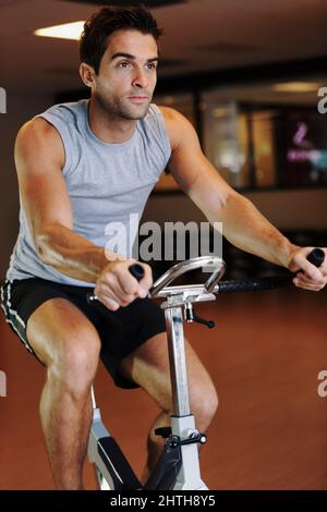 Portando il suo ciclismo a un nuovo livello. Un bel giovane uomo che indossa abbigliamento sportivo e utilizza una bicicletta da ginnastica in palestra. Foto Stock