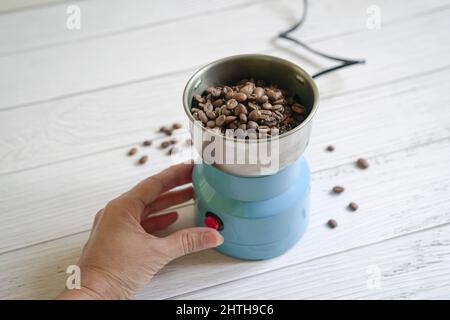 Chicchi di caffè all'interno di un macinacaffè elettrico, con la mano della donna accanto. Spazio di copia. Foto Stock