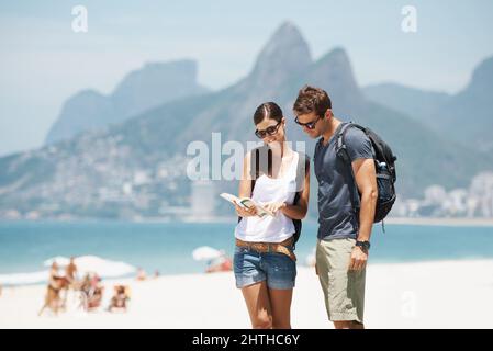 Ottenere i nostri cuscinetti in paradiso. Scatto di una giovane coppia che guarda una mappa mentre si trova su una spiaggia. Foto Stock