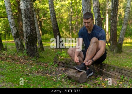 Uomo che lega le sue scarpe nel parco all'aperto, intorno alla foresta, querce erba verde giovane atleta di perseverante. Atleta attivo natura, allenamento Foto Stock