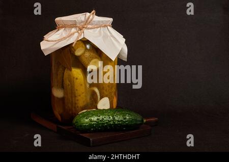 Un vaso di vetro con cetrioli sottaceto e cetrioli freschi su un supporto di legno Foto Stock