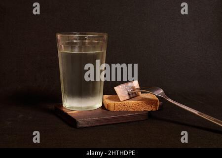 Vetro sfaccettato di vodka, pane di segale e aringhe su una forchetta su un supporto di legno Foto Stock