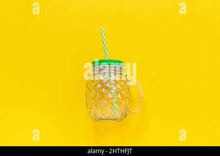 Vasetto di vetro vuoto in forma di ananas con coperchio verde e paglia per frullati di frutta o verdura, cocktail e altre bevande su sfondo giallo. Da a. Foto Stock