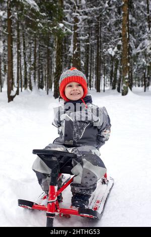 un ragazzo felice in discesa su una slitta in inverno, un bambino in abiti luminosi siede su una slitta, la neve lo vola Foto Stock