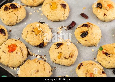 Refrigerazione di biscotti di farina d'avena appena sfornati con uvetta, frutta candita, semi di lino e sesamo e noci su carta da forno Foto Stock