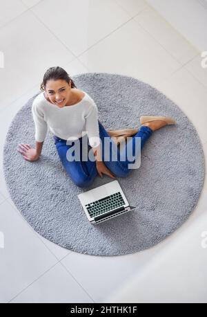 Ive ha avuto tutto il mondo a portata di mano. Vista dall'alto di una graziosa bruna con il suo computer portatile mentre si siede sul pavimento. Foto Stock