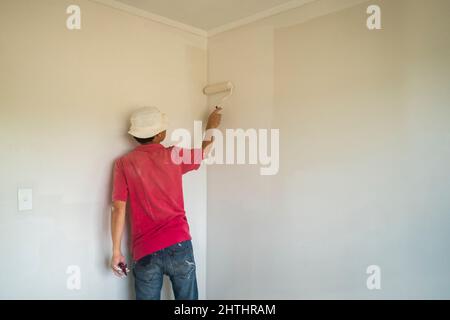 Uomo che dipinge le pareti in una nuova casa con un rullo Foto Stock