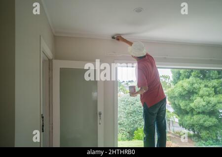 Uomo che dipinge il muro sopra la finestra con un pennello Foto Stock