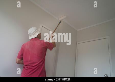 Uomo che dipinge soffitto con un rullo in nuova casa Foto Stock