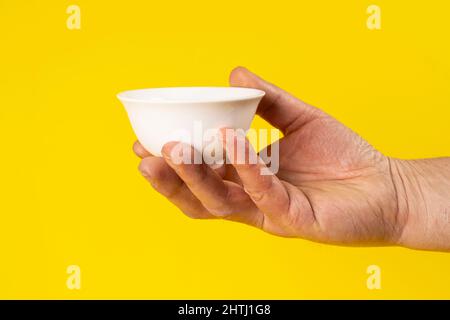 una piccola ciotola in ceramica bianca in mano di un uomo su sfondo giallo Foto Stock