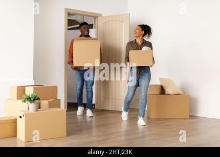 Felice coppia nera che entra nella nuova casa che trasporta le scatole di cartone all'interno Foto Stock