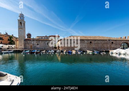 Porto di Lazise con piccole barche ormeggiate e l'antica chiesa di San Nicolò in stile romanico. Località turistica sulla costa del Lago di Garda. Foto Stock