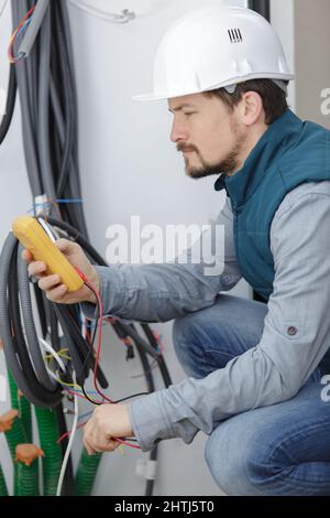 elettricista che misura la tensione nella presa in ambienti chiusi Foto Stock