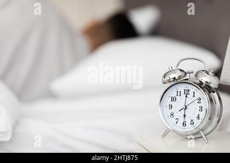 Sveglia sul comodino e vista offuscata della giovane donna che non vuole  svegliarsi, coprendo le orecchie con cuscino nel letto Foto stock - Alamy