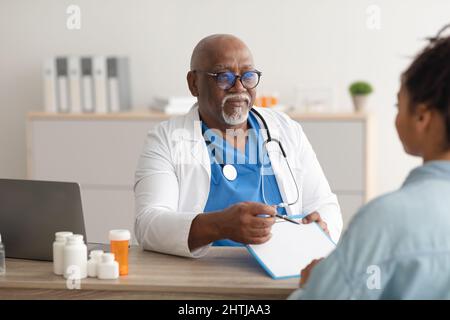 Medico esperto di colore che spiega il piano di trattamento alla paziente femminile Foto Stock