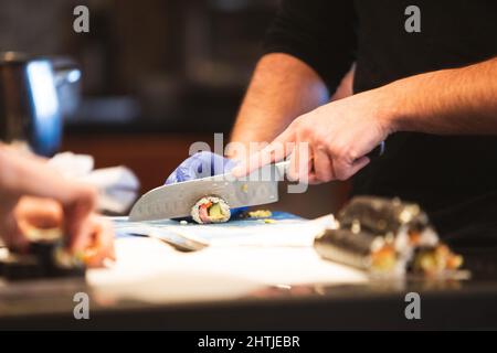 Una persona che taglia un rotolo di sushi con un coltello Foto Stock