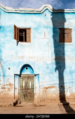 Esterno di vecchia casa con pareti dipinte di blu e porta shabby con piccole finestre situato sulla strada soleggiata della città Foto Stock