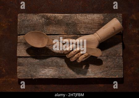 Vista dall'alto della mano di manichino artificiale con un grande cucchiaio di legno posto su un tagliere vecchio stile in una stanza luminosa Foto Stock