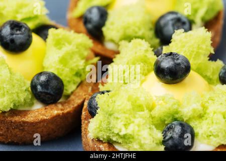 Torte dolci con gustosi biscotti verdi ricoperti di mirtilli maturi serviti sul piatto in camera luminosa Foto Stock