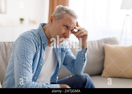 Stressato uomo maturo seduto sul divano e pensando Foto Stock
