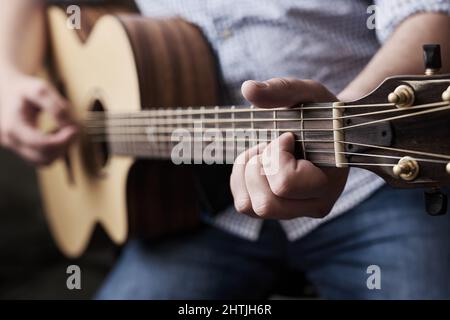 La pratica rende perfetto. Scatto corto di un uomo irriconoscibile che suona una chitarra acustica a casa. Foto Stock