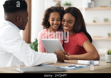 Madre nera e figlia in visita pediatra, in possesso di tablet digitale Foto Stock