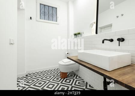 Bagno moderno con pavimento idraulico bianco e nero con lavandino in porcellana bianca, piastrelle bianche e rubinetti neri Foto Stock