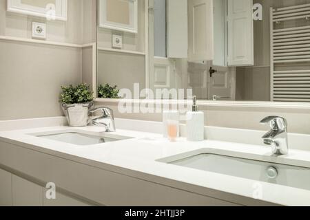 Lavandino monopezzo con due lavandini e due rubinetti in bagno con specchio a muro e radiatore bianco per asciugamano Foto Stock