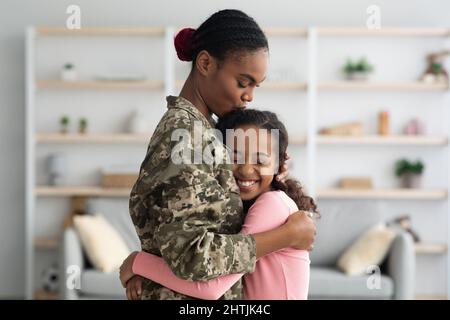 Vista laterale della madre nera in uniforme militare abbraccia il bambino Foto Stock
