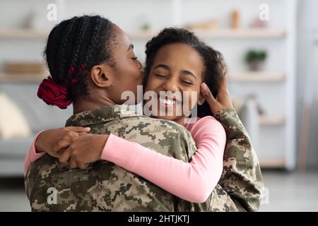 Amorevole madre nera in uniforme militare baciare figlia Foto Stock