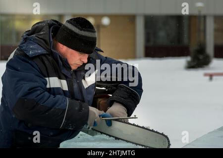 Un file manuale lavoratore acuisce una motosega catena Foto Stock